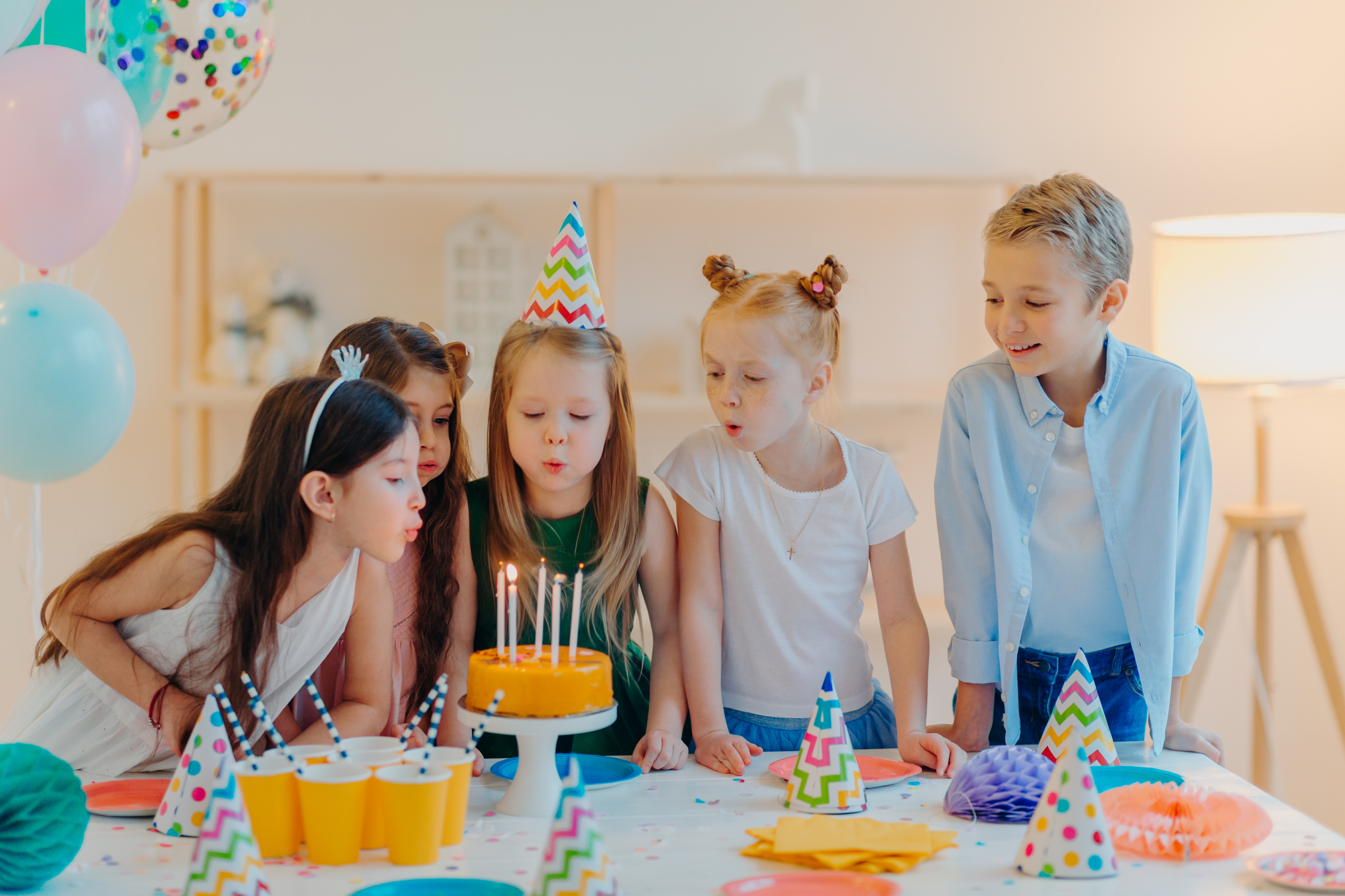 Small kids celebrate birthday party, blow candles on cake, gather at festive table